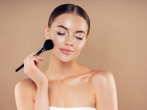 Beautiful young woman applying foundation powder